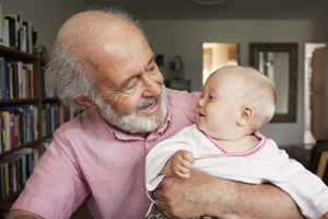 A senior man and baby boy smiling at home.